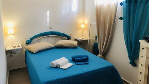 Un dormitorio con cama, dos mesitas de noche, lámpara, cortina y un mueble pequeño.