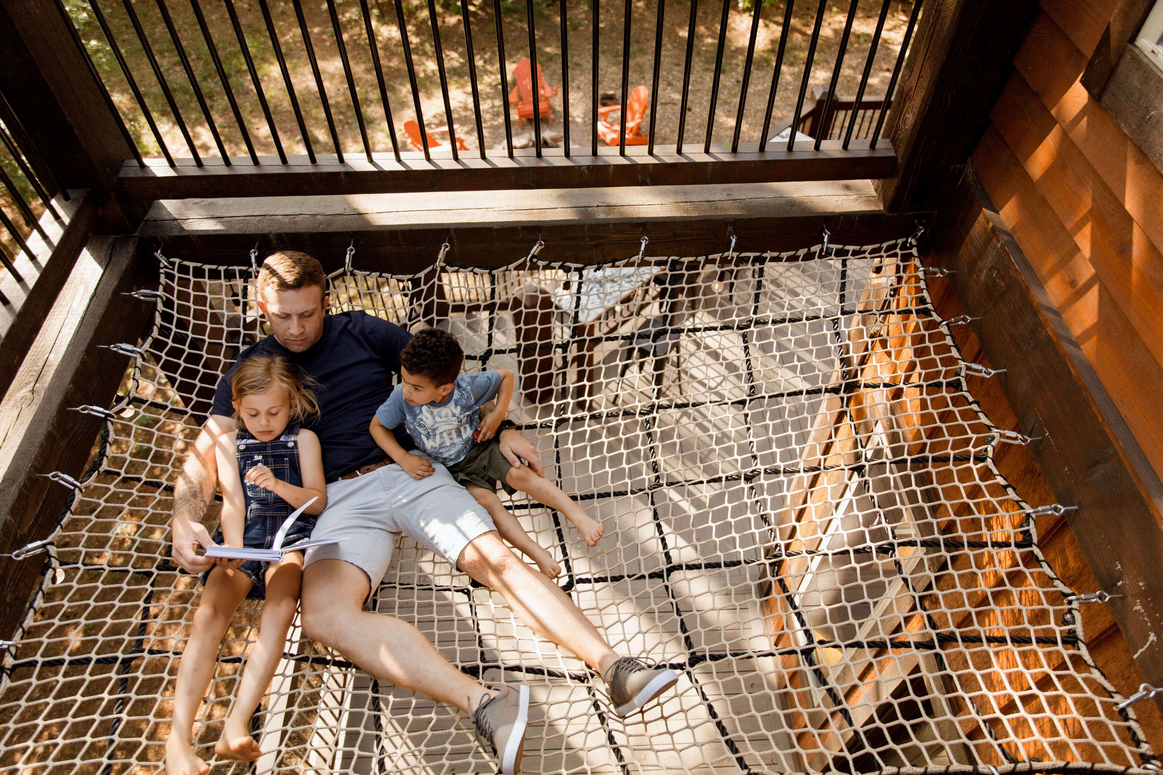 A hammock with three people lying on it, surrounded by a wooden structure with a metal fence.