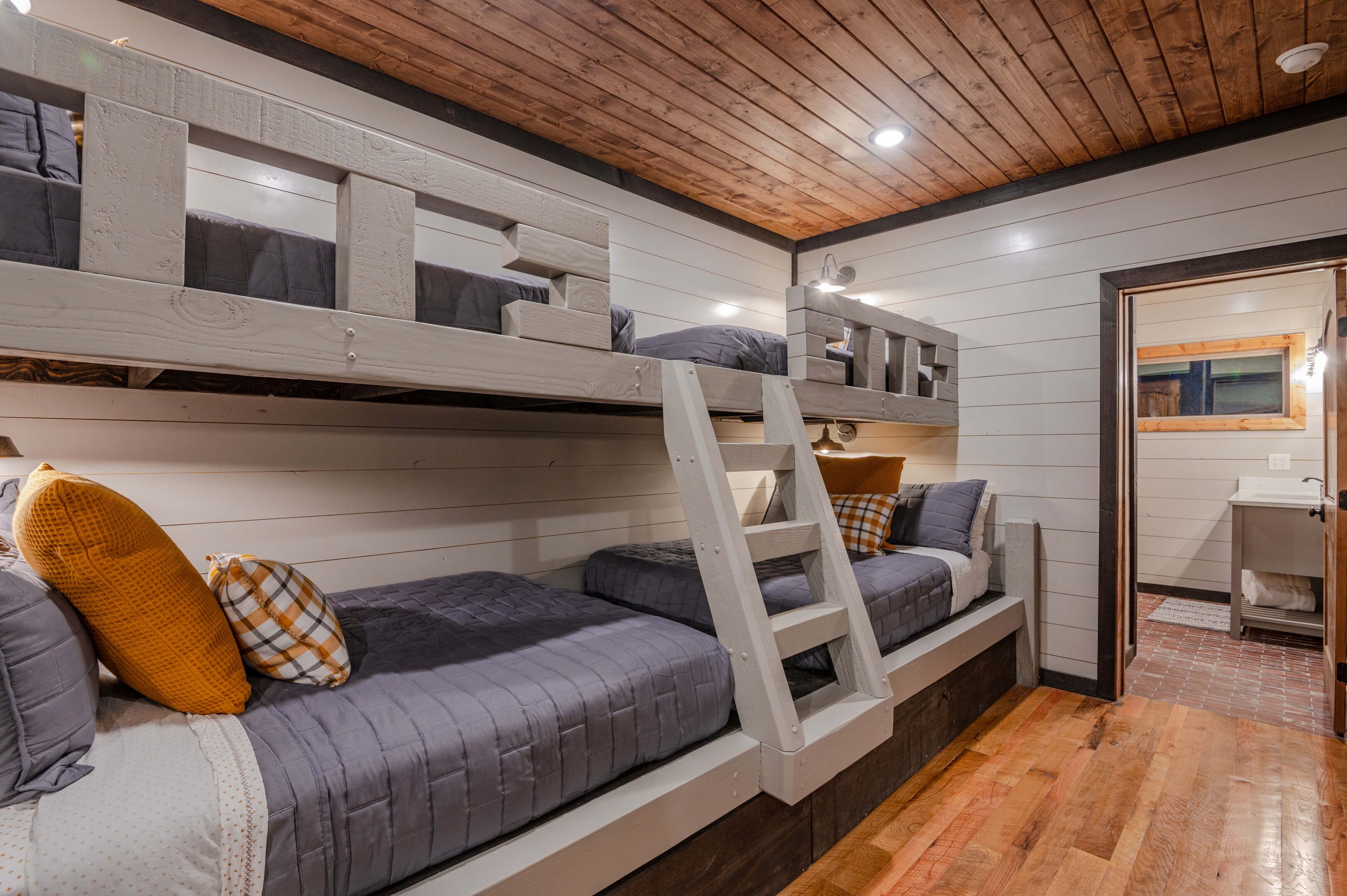 Une chambre avec un lit superposé, des poutres en bois, une échelle et un petit bureau avec une lampe.