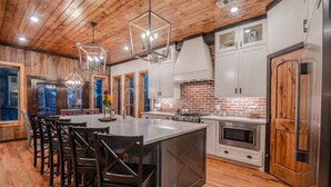 Una cocina moderna con una isla grande, armarios blancos y un respaldo de ladrillo.