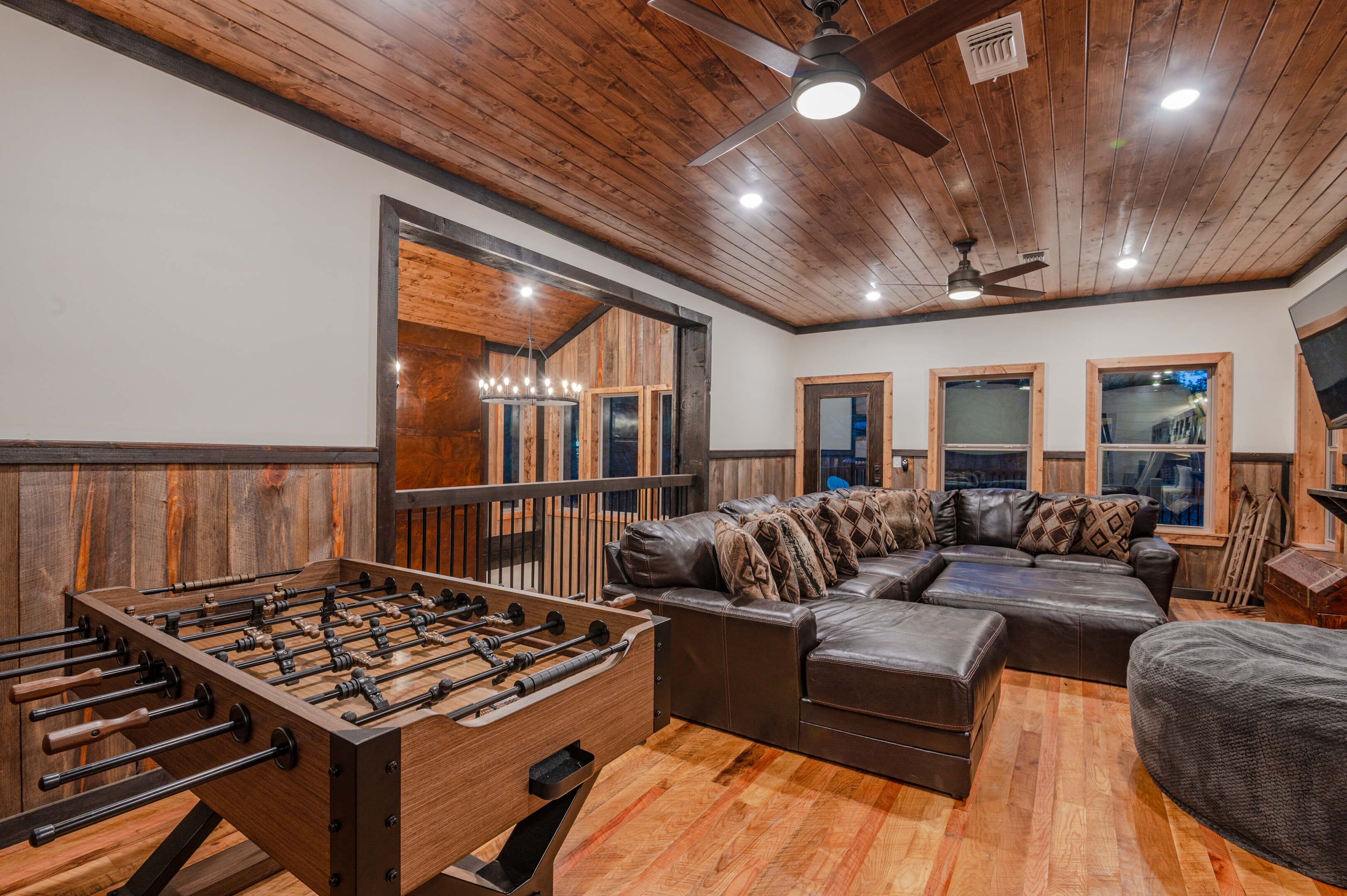 A cozy living room with a foosball table, a sectional sofa, and a ceiling fan.