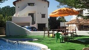 Zona de piscina con un edificio blanco, mobiliario exterior y una sombrilla.