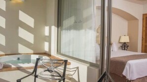 A hotel room with a bed, a small table, a chair, a bathtub, and a window with blinds. - Club Regina Grand 2! (Marina Vallarta)
