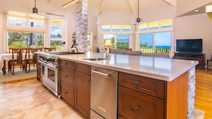 A spacious kitchen with a large island, built-in oven, and refrigerator. There are multiple windows offering views of the outdoors.
