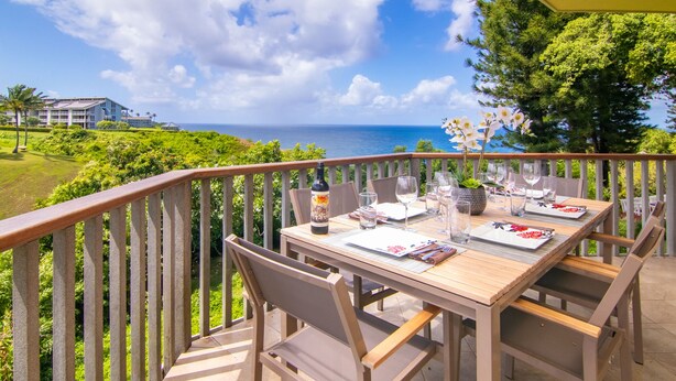 An outdoor dining area with a wooden table set for four, overlooking a scenic ocean view.