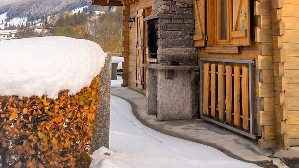 A wooden cabin with a stone chimney, a snow-covered roof, and a view of a snowy landscape. - Homerez - Chalet in La Bresse (La Bresse)