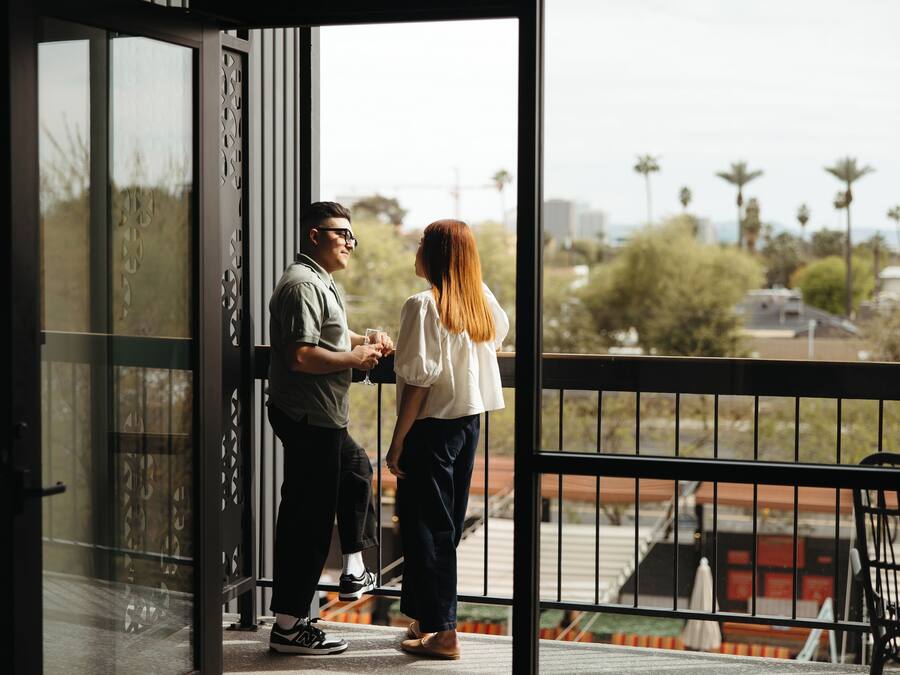 Una pareja parada en un balcón con vistas a palmeras y edificios.