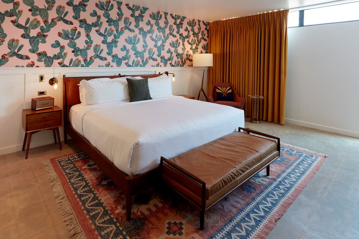A hotel room with a large bed, a bedside table with a lamp, a chair, and a patterned rug.