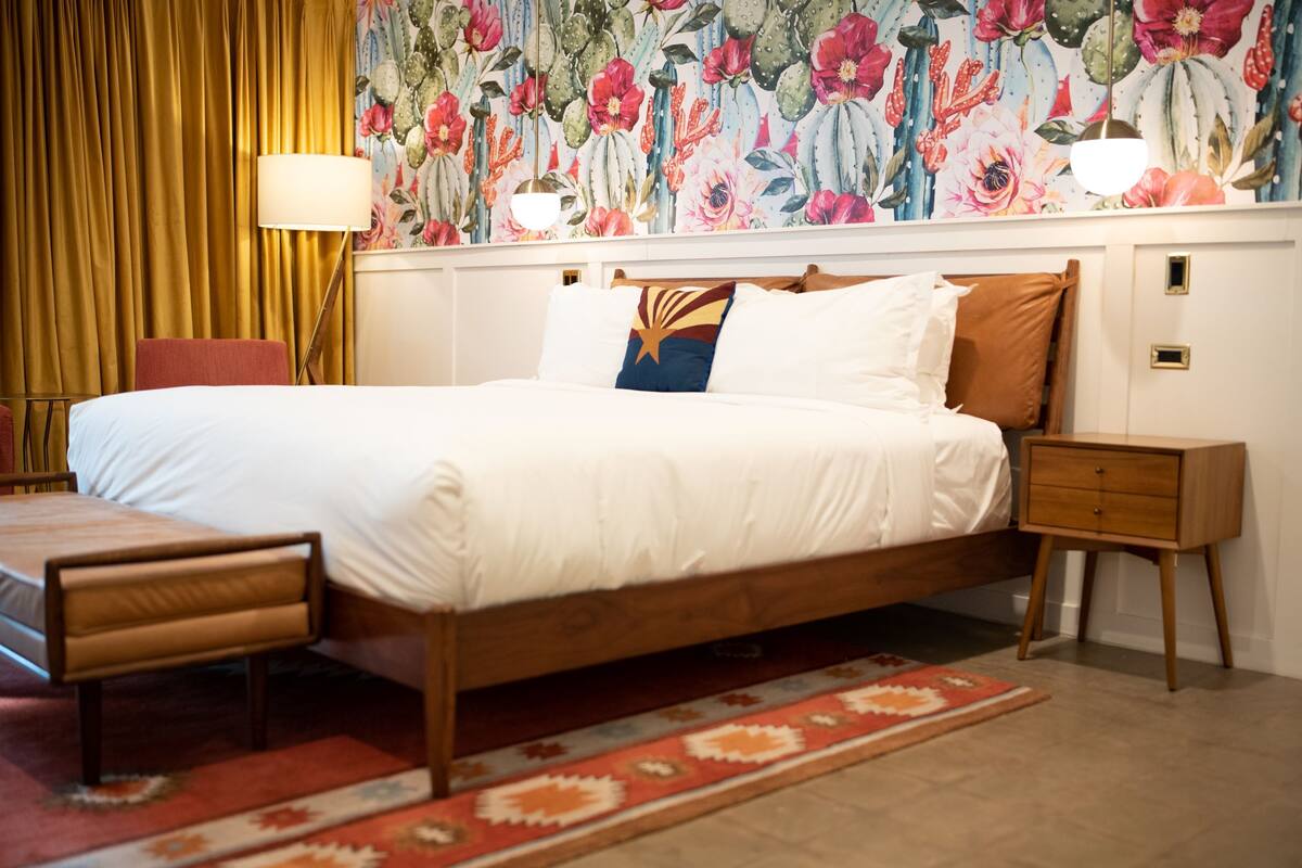 A neatly arranged bedroom with a large bed, bedside tables, a nightstand, and a floral wallpaper.