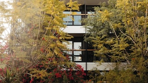 Un edificio moderno de varios pisos, rodeado de follaje denso y plantas con flores.