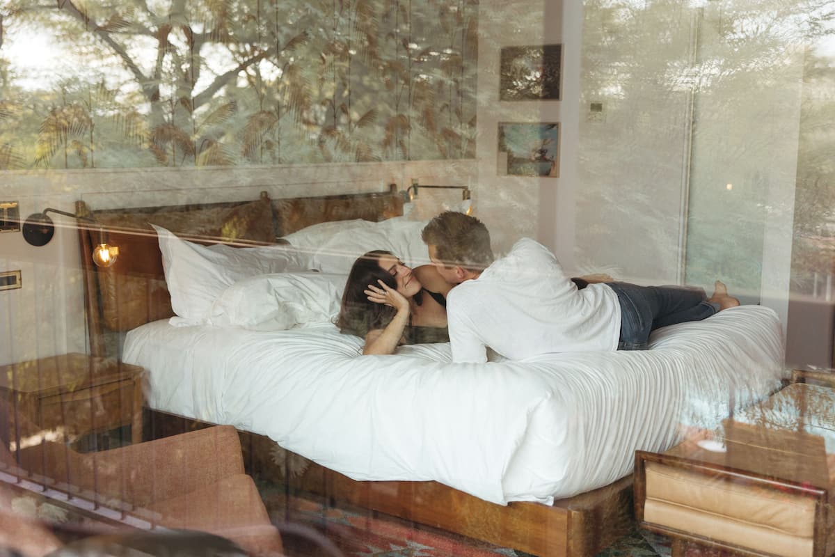 A bedroom with a wooden headboard, a large window with a view of trees, and a bedside table with a lamp.