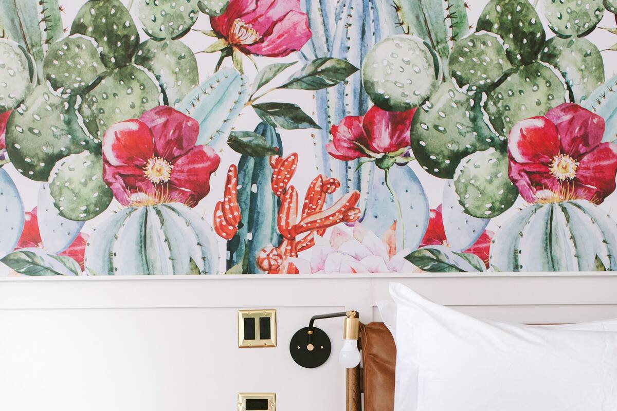 A bedroom with a bed, a nightstand, a wall-mounted lamp, and a cactus-themed wallpaper.