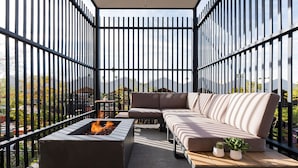 Un área de estar moderna al aire libre con un brasero, un sofá y dos plantas en macetas.