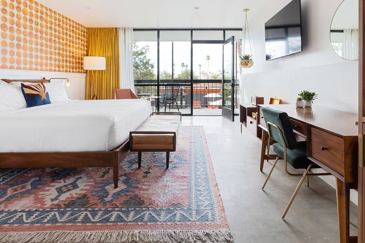 A hotel room with a large bed, a desk, a chair, and a balcony with a view.