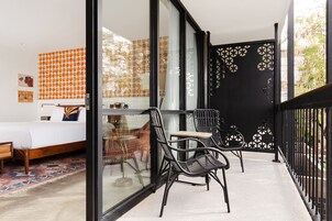 Un balcone con una porta in vetro, un letto con parete decorata e due sedie nere.