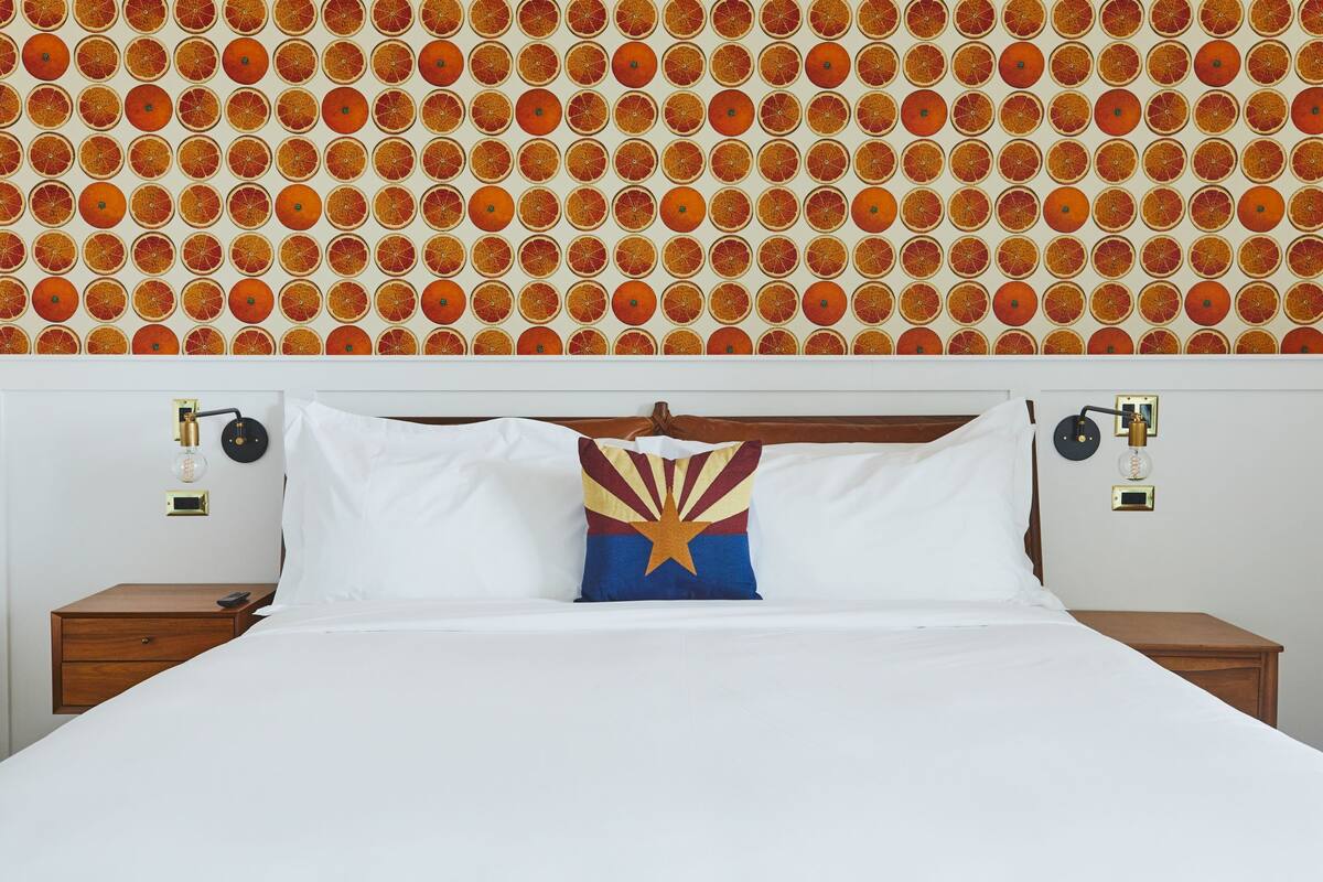 A hotel room with a bed, white bedding, a pillow with a star design, and a wall with a circular pattern.