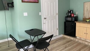 A compact kitchen with a white door, a small dining table with two chairs, a microwave, and a refrigerator. - Pet-Friendly 1BR Sarasota Florida Vacation Rental, Patio, Near Beaches, 2 Guests (Sarasota)