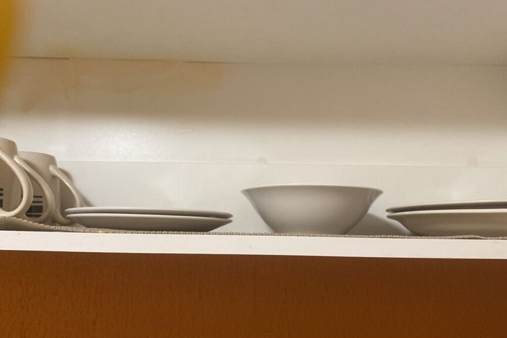Ett kök med vita skåp och en vit bänkskiva. På bänkskivan står tre vita skålar och en vit tallrik.