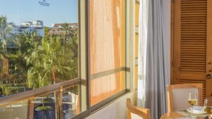 Une pièce avec vue sur les palmiers et les immeubles, une porte en bois et une table avec des verres à vin.