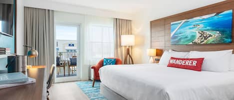 A hotel room with a large bed, a desk, a chair, a view of the sea, and a painting of a beach scene.