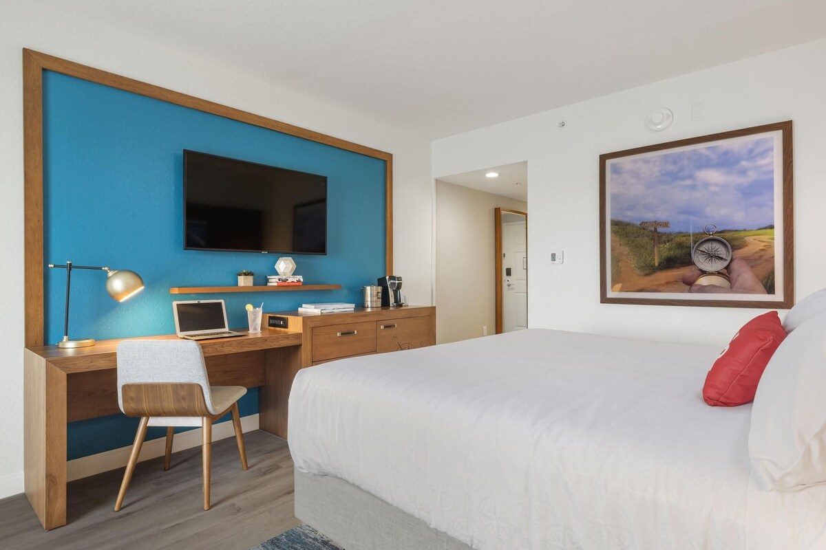 Een hotelkamer met een bed, bureau, stoel, televisie en een schilderij.