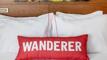 Hotelkamer met een groot landschap op de muur en een rood kussen met het woord 'WANDERER' op het bed.
