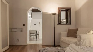 A bedroom with a bed, a bedside table, a floor lamp, and a mirror on the wall. - GuestHost - Rione Monti & Fori Imperiali Elegant Apartment x3 (Roma)