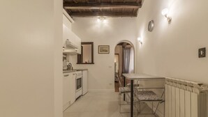A narrow hallway with a kitchen on the left, a dining table with chairs in the center, and a radiator on the right. - GuestHost - Rione Monti & Fori Imperiali Elegant Apartment x3 (Roma)