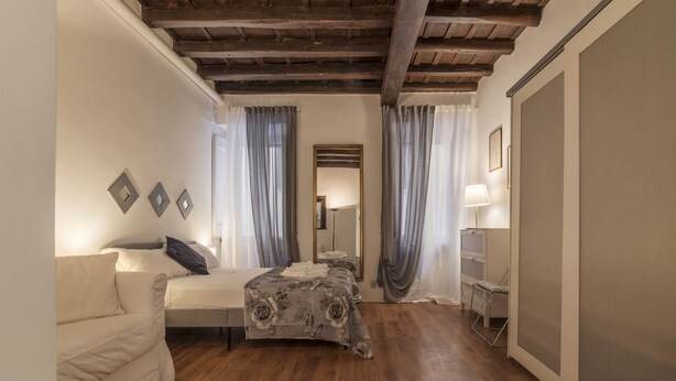 A bedroom with a bed, a sofa, a mirror, and a window with curtains. - GuestHost - Rione Monti & Fori Imperiali Elegant Apartment x3 (Roma)