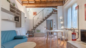 Un espacio habitable moderno con un sofá azul, una mesa redonda, sillas transparentes, una escalera y un extintor.