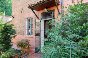 A brick building with a wooden pergola, a metal gate, and a garden area with potted plants.