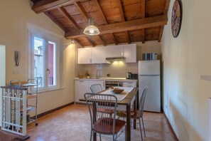 A kitchen with white cabinets, a wooden ceiling, a dining table with chairs, and a window with a view.