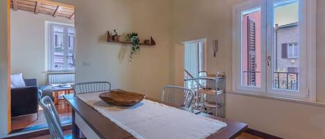 A dining area with a wooden table, chairs, a white table runner, and a hanging plant.