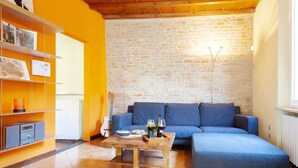 A living room with a blue sofa, a wooden coffee table, and a guitar against a brick wall. - GuestHost - Ferrara Lilac Casa dell'Archivòlto with Garage (Ferrara)