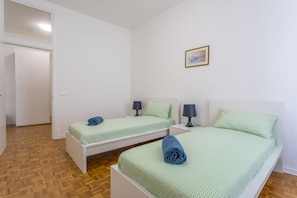 A room with two beds, each with a pillow and a lamp, a framed picture on the wall, and a wooden floor. - GuestHost - NEW! Ricasoli Garden Modern Apartment x5 (Udine)