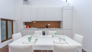 A modern kitchen with white cabinets, a dining table set for four, and a window providing natural light. - GuestHost - NEW! Ricasoli Garden Modern Apartment x5 (Udine)