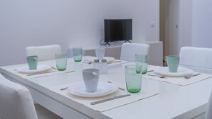 A dining table set with plates, cups, and cutlery, a flat-screen TV mounted on the wall, and a white chair. - GuestHost - NEW! Ricasoli Garden Modern Apartment x5 (Udine)