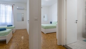 A room with two beds, a mirror, an air conditioning unit, and a wooden floor. - GuestHost - NEW! Ricasoli Garden Modern Apartment x5 (Udine)