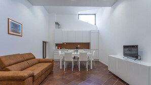A modern interior with a sofa, dining table, chairs, a TV, and a kitchen area. - GuestHost - NEW! Ricasoli Garden Modern Apartment x5 (Udine)