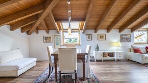 Una habitación en el ático con techo de madera, una mesa de comedor con sillas, un sofá y un armario blanco.