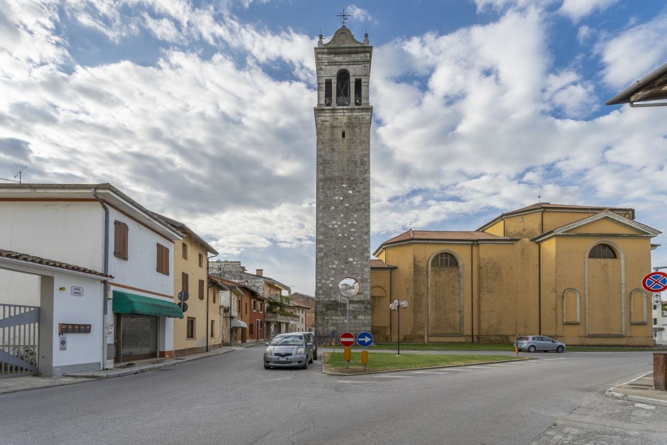 Une rue bordée d’une haute tour, d’une église et d’un bâtiment doté d’un auvent vert.