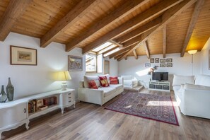 A spacious living room with wooden beams, white furniture, and a large window.