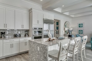 A modern kitchen with white cabinetry, a granite island, and a dining area with white chairs.