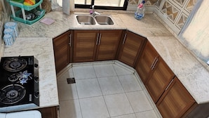 A kitchen with wooden cabinets, a double sink, a stove, and a tiled floor. - Jerash Inn (Jerash)