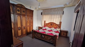 A bedroom with a wooden bed, a wardrobe, a nightstand, and a ceiling light fixture. - Jerash Inn (Jerash)