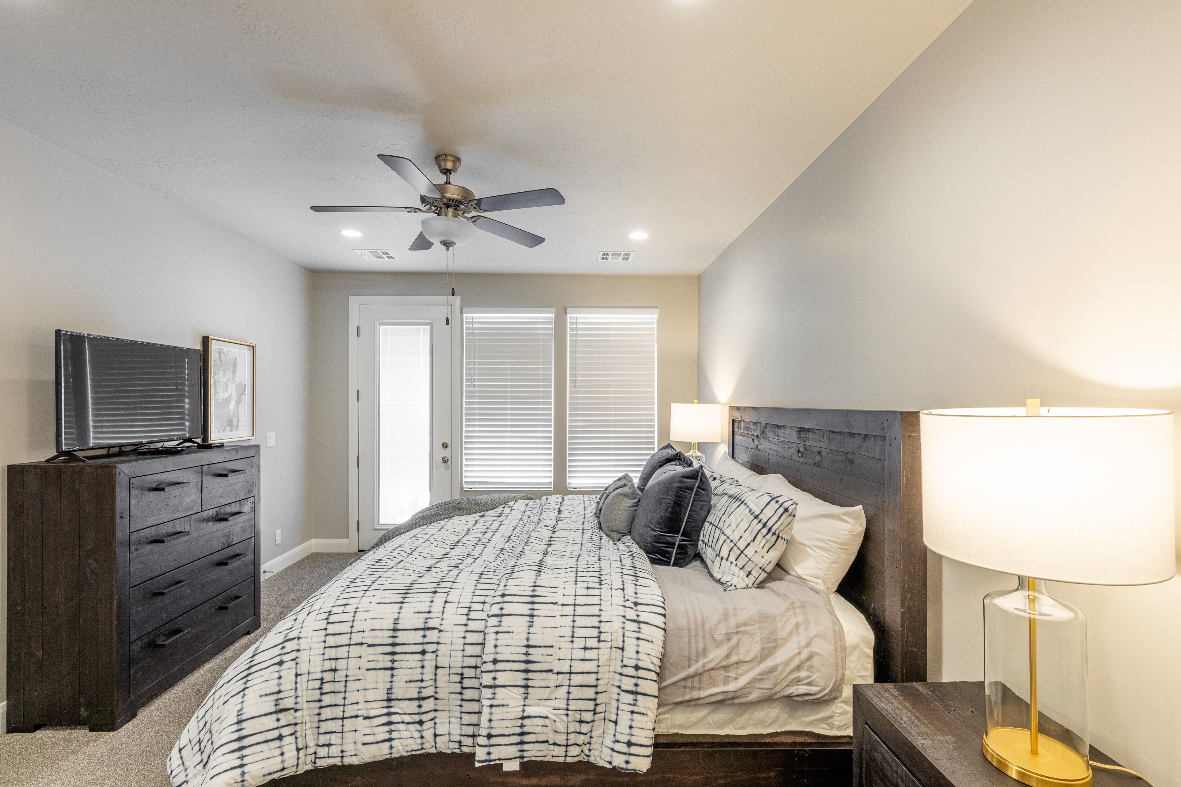 A bedroom with a bed, dresser, ceiling fan, and bedside lamp.