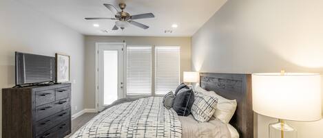 A bedroom with a bed, dresser, ceiling fan, and bedside lamp.
