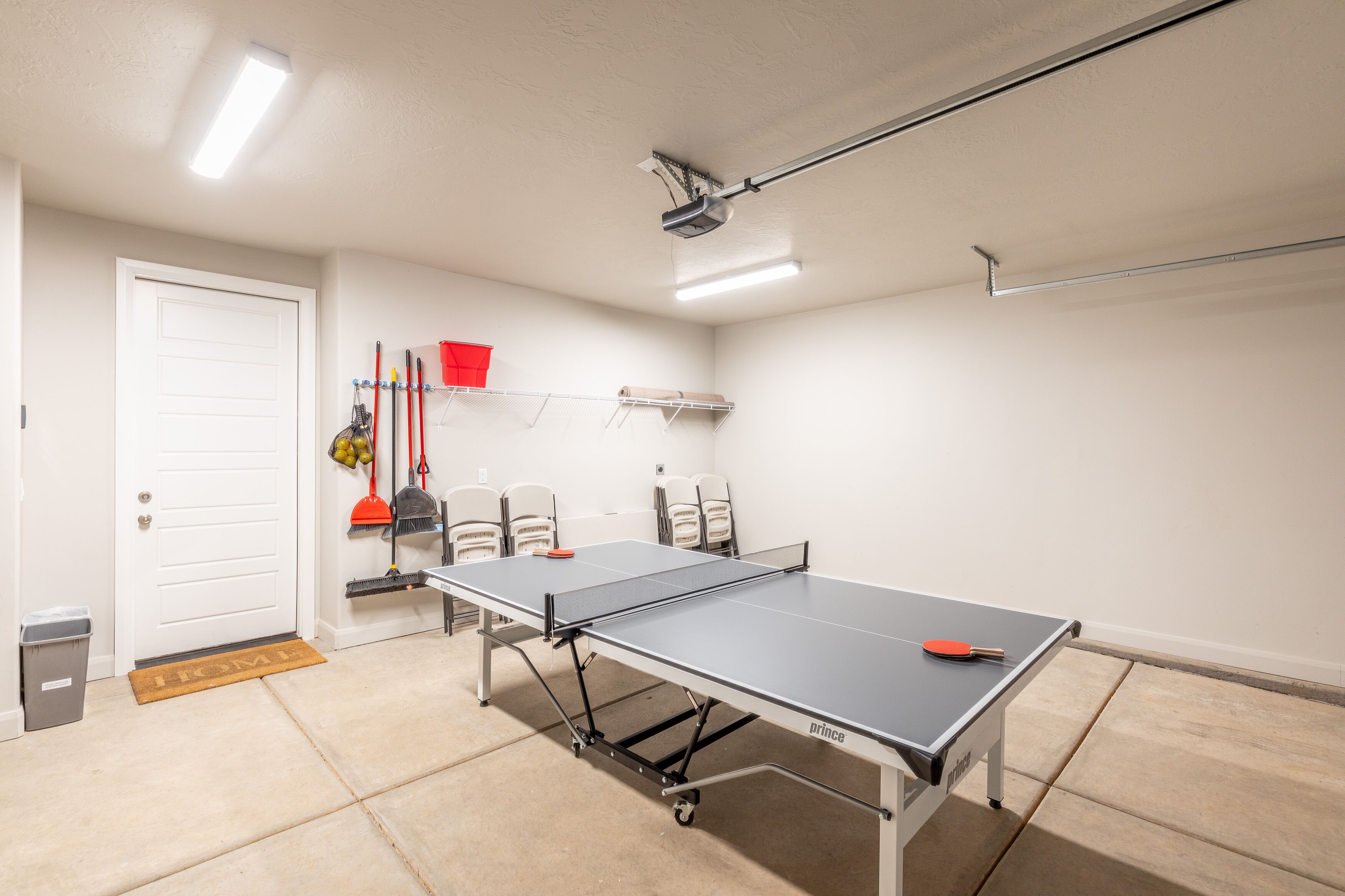 A ping pong table in a room with a white door, a trash bin, and a doormat.