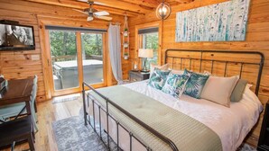 A wooden cabin bedroom with a bed, a desk, a chair, a ceiling fan, and a view of the outdoors. - Luxurious Log Cabin with Stunning Views (Sugar Mountain)