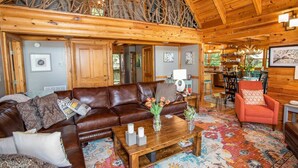 A spacious living area with a high ceiling, wooden beams, a leather sofa, a red armchair, and a coffee table with decorative items. - Luxurious Log Cabin with Stunning Views (Sugar Mountain)